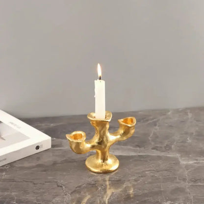 Gold resin candle holders featuring a textured organic design with three arms holding one lit white candle centerpiece