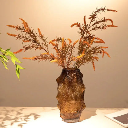A textured amber sea cucumber glass vase with an organic form holding dried orange and brown foliage for decor