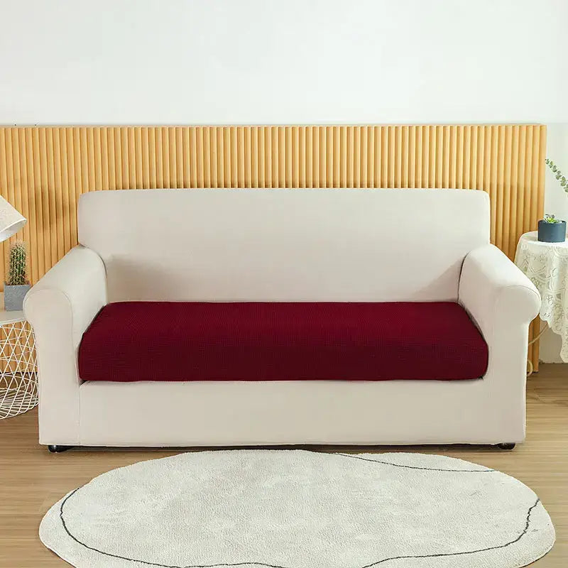 Cream-colored stretch sofa cover with deep red seat cushion fitted over textured green waterproof elastic sofa cover