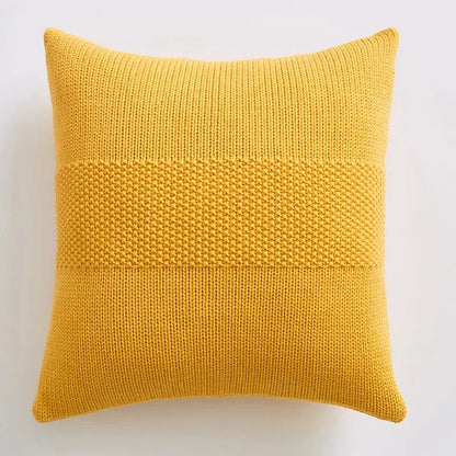 A square mustard-yellow knitted throw pillow with textured knit cushion cover and two horizontal denser stitch bands