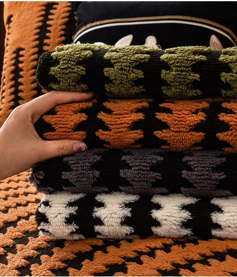 Stack of cozy knit sofa covers with bold geometric patterns in olive black, white black, gray black, and orange black colors