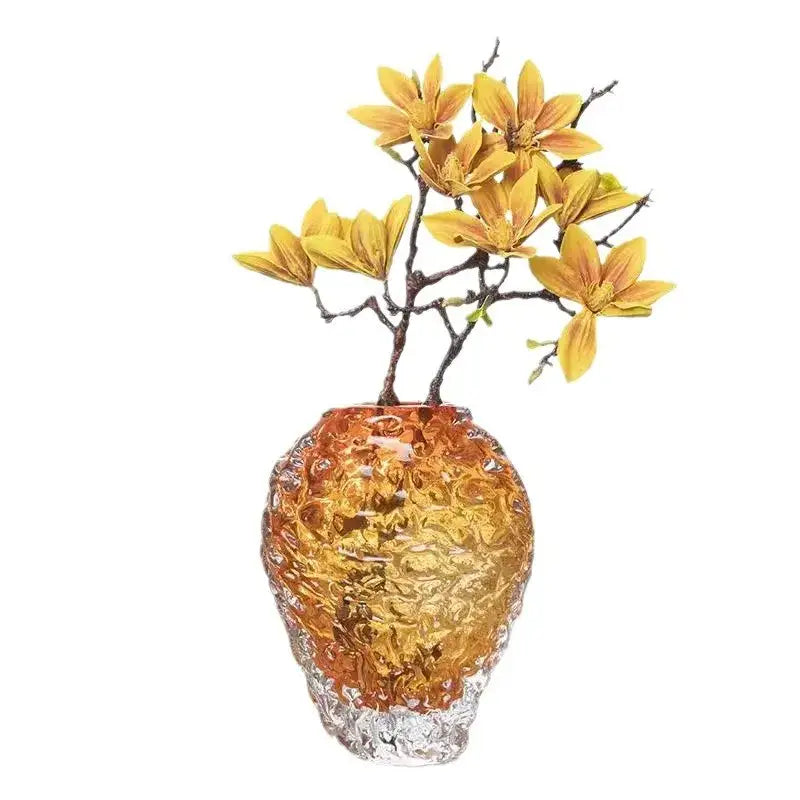 Textured amber glass colored vase with clear base holding artificial yellow magnolia blossoms for living room decor