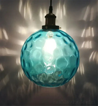 Textured turquoise blue glass ball pendant light with hammered bubble texture and dark metal fixture for kitchens