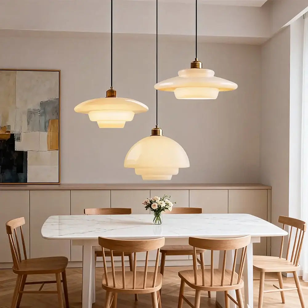 Three tiered cream glass pendant lights with brass and nickel finish hang above a marble dining table