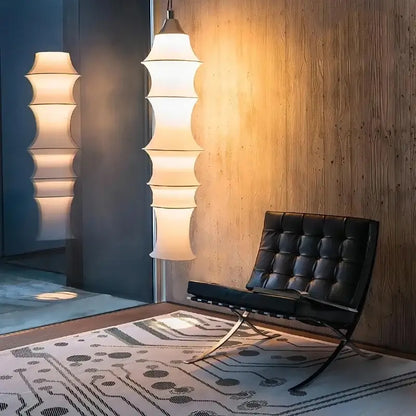 Black leather tufted chair with chrome x-frame legs beside decorbites cream silk tiered japanese floor lamp for living room lighting