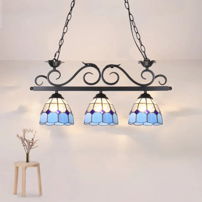 Blue stained glass pendant light fixture with ornate black metal frame and curved bird shape by DecorBites