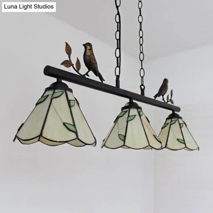 Three-tiered tiffany style pendant light with cone stainless glass shades, bird accent, and black wrought iron frame for island lighting