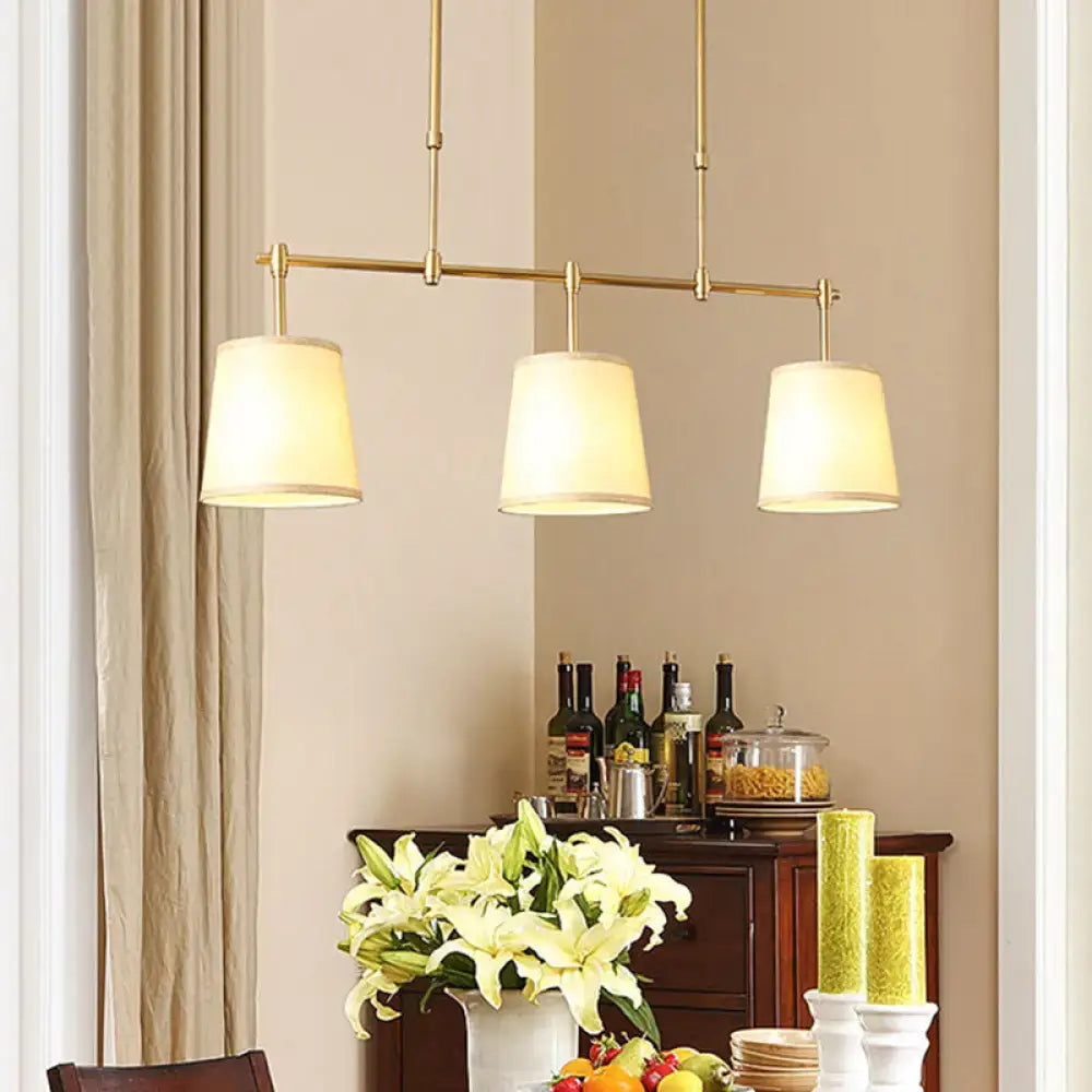 Brass-finished three-light pendant lighting with cream fabric shades ideal for dining room or barrel island light use