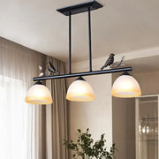 DecorBites™ black metal ceiling light with three white glass shades and decorative bird figurines for dining room island