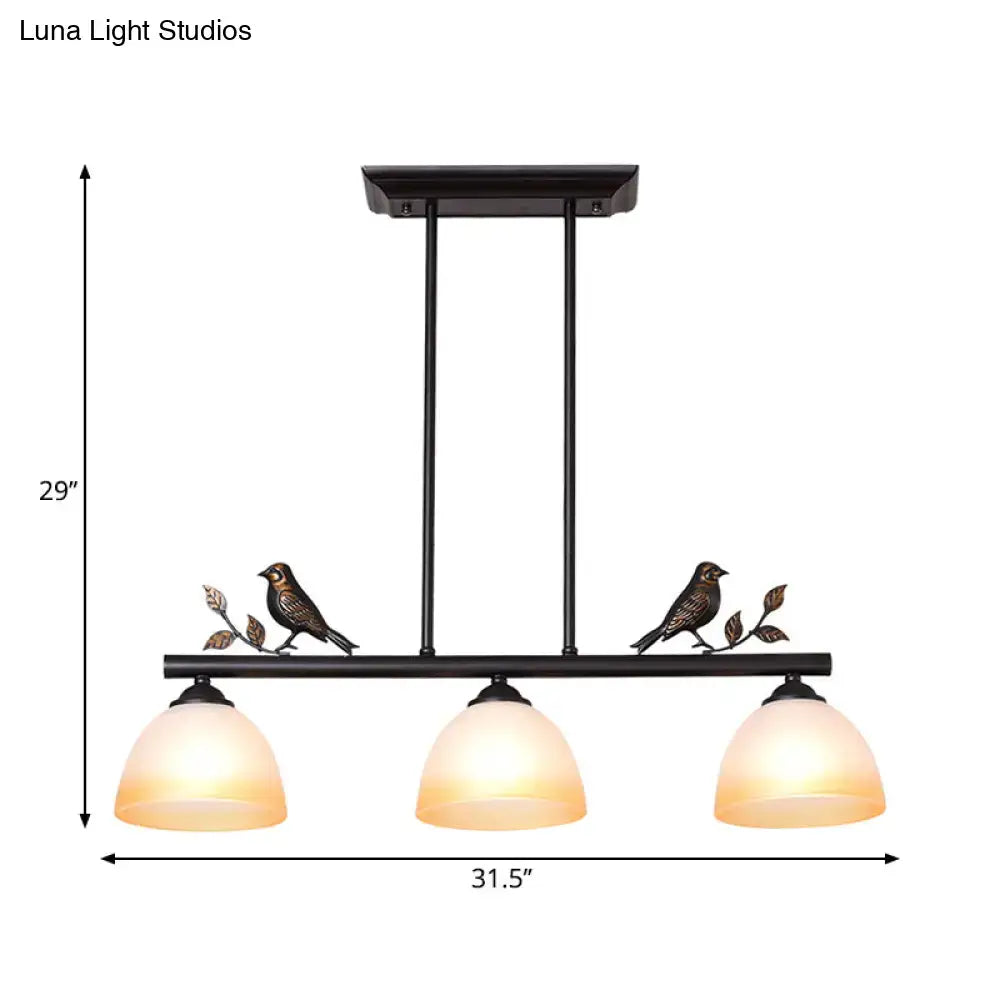 Black metal ceiling light with three warm white glass shades and decorative bird figurines on branches for dining room island