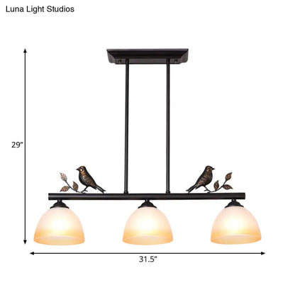 Black metal ceiling light with three warm white glass shades and decorative bird figurines on branches for dining room island