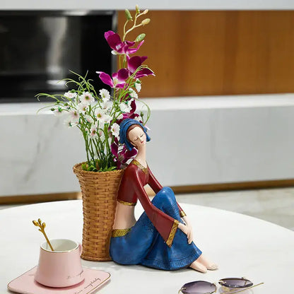 A ceramic resin ornament of a woman in a blue and red dress with gold trim beside a basket of purple flowers for cute girls storage
