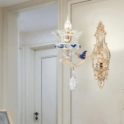 Elegant gold-toned brass wall sconce light with clear glass flower design blue bird motif and dangling crystal teardrop