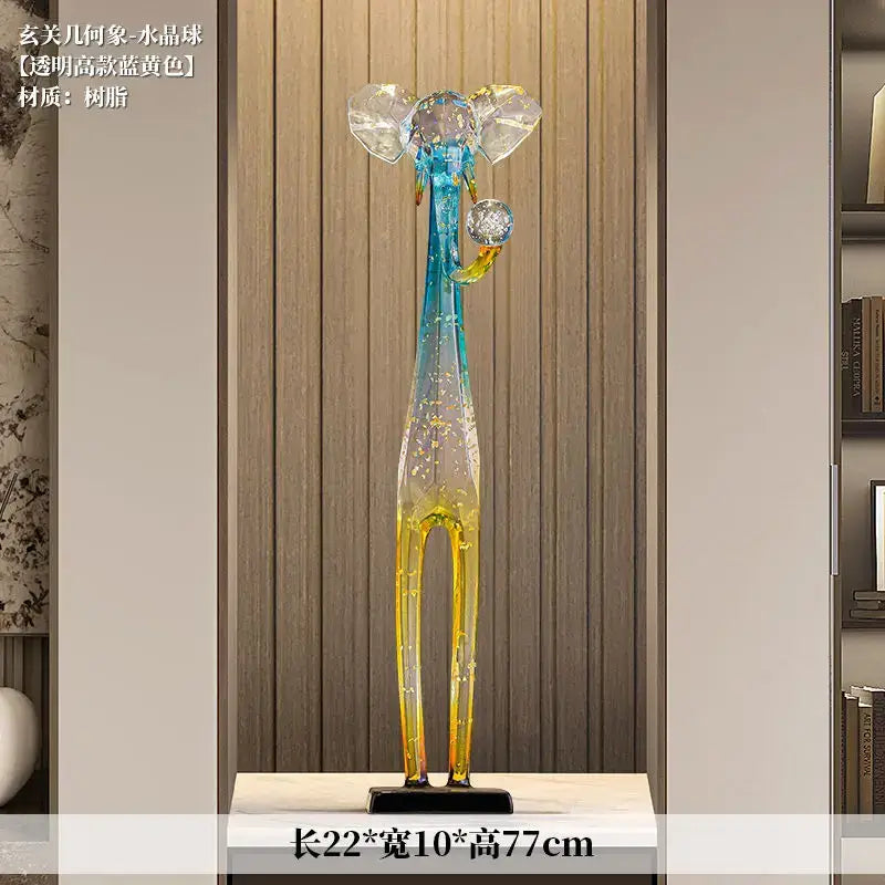 A tall translucent blue and yellow elephant floor decoration sculpture with crystal-like ears and trunk holding an ornament