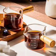 Transparent glass espresso measuring cups with wood handle filled with dark amber liquid for precise measuring