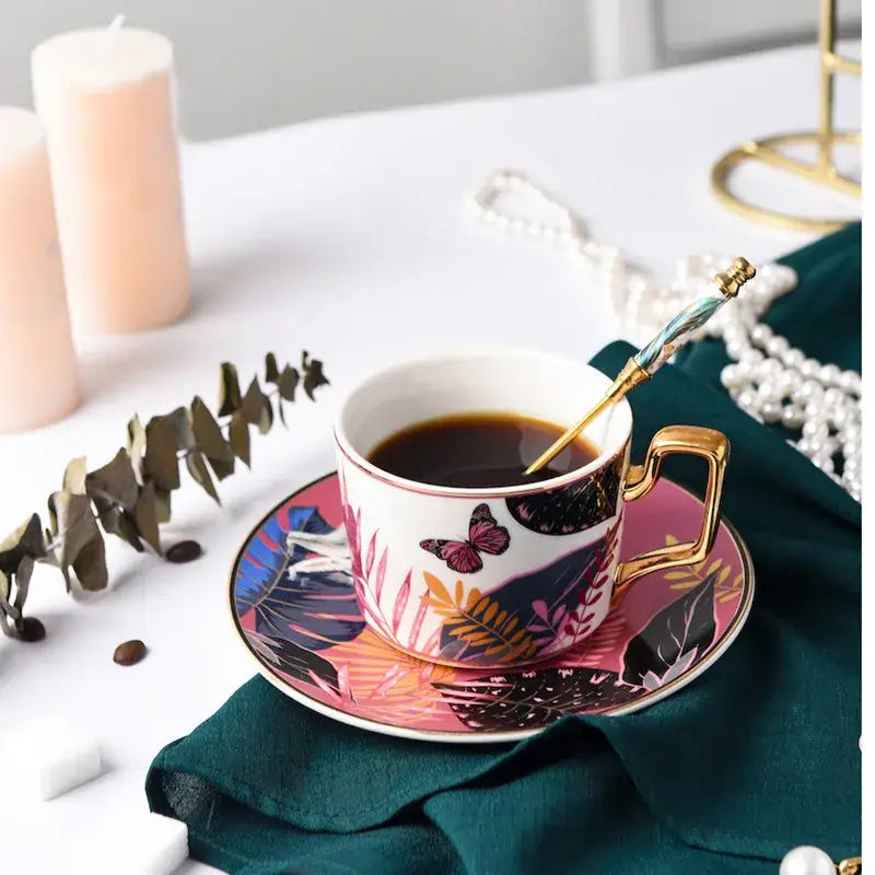 White ceramic tea cup set with gold handle and tropical leaf butterfly design on matching saucer for dining room