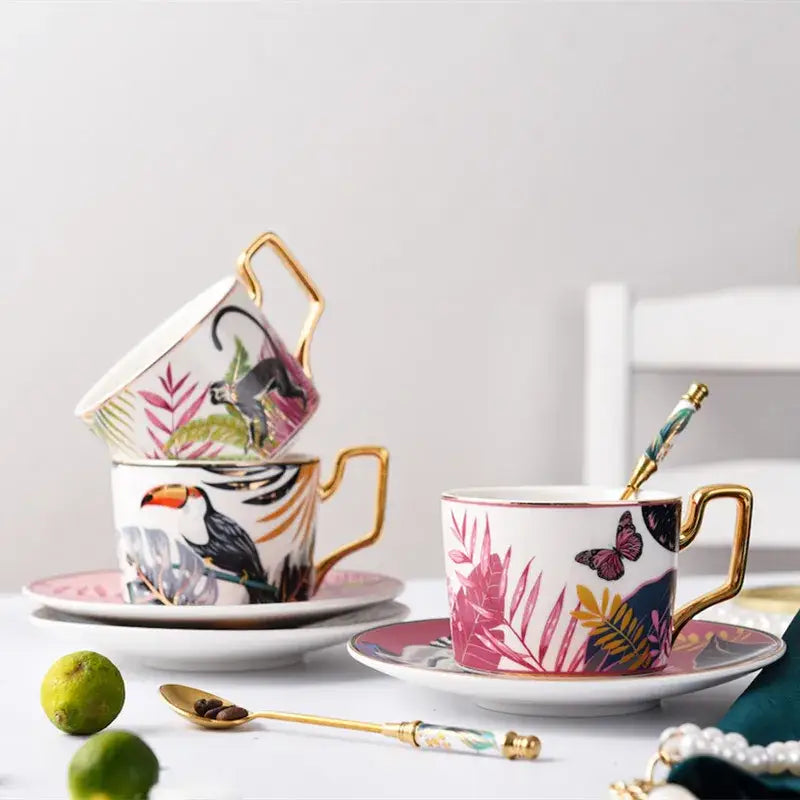 A tropical pink and black toucan porcelain tea cup set with gold handles and matching saucer featuring bold foliage