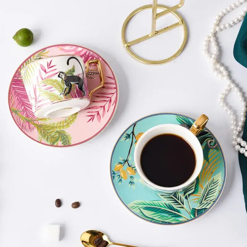 White ceramic tea cup with gold handle and black monkey design on pink tropical leaf saucer in tea cup set