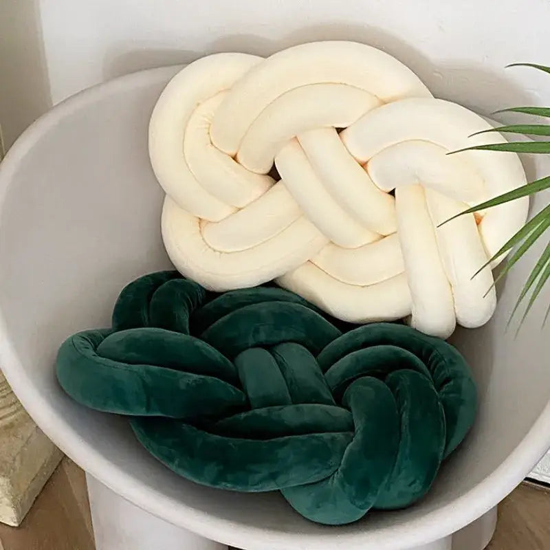 Cream-colored and deep green velvet knot throw pillows crafted from plush fabric with a braided design for living rooms