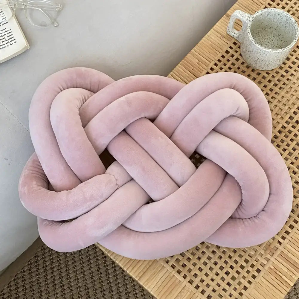 A dusty rose-colored knot throw pillow made of soft suede-like fabric for living room decor