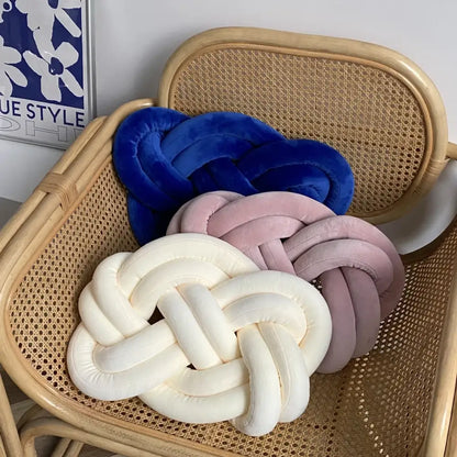 Three velvet knot throw pillows in royal blue soft pink and creamy white on a woven rattan chair for living room decor
