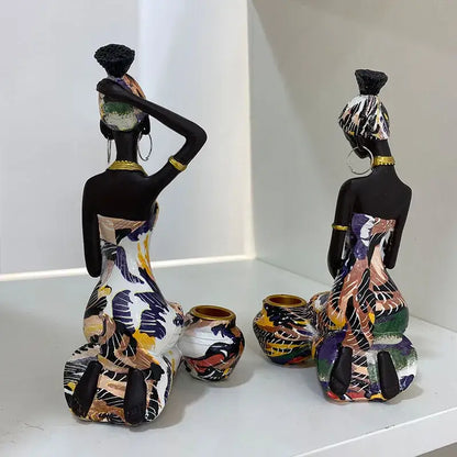 Two stylized decorbites black woman candlestick figurines with black painted skin and colorful dresses on white shelf