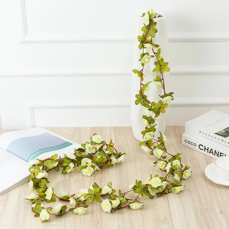 A delicate flowers vine garland featuring cream-colored rose flowers and green leaves on thin stems for decor
