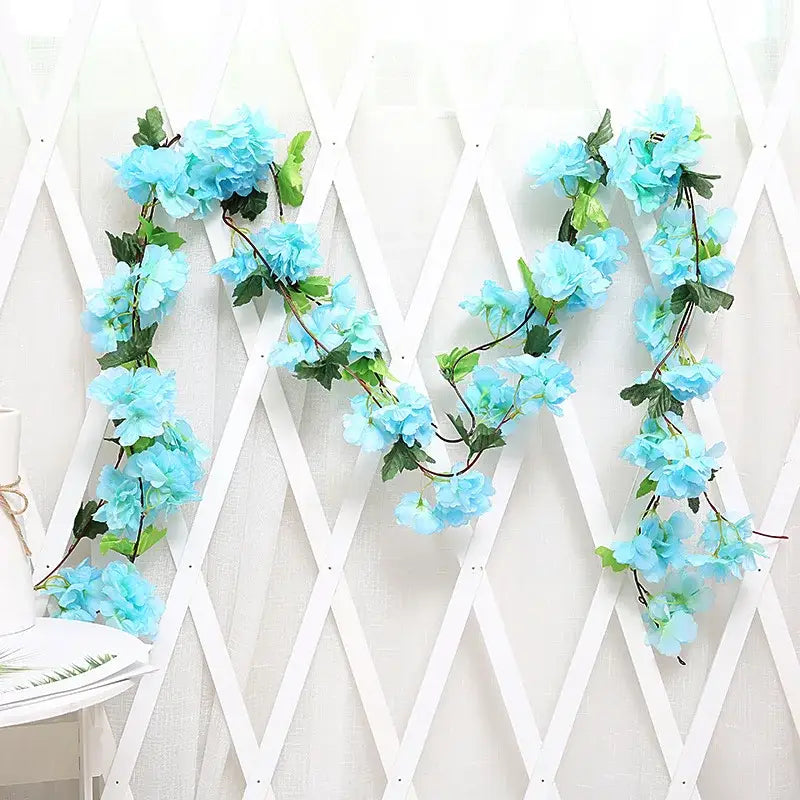 Light blue artificial hydrangea rose flowers vine garland with green leaves and dark stems on white lattice backdrop