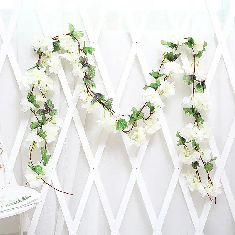 A delicate white artificial rose flowers vine garland with green leaves and brown stems for living room decor