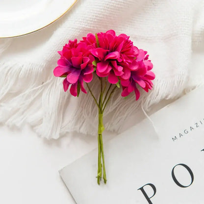 A vibrant fuchsia artificial flower stamen bouquet with layered petals and green stems on a white textured surface