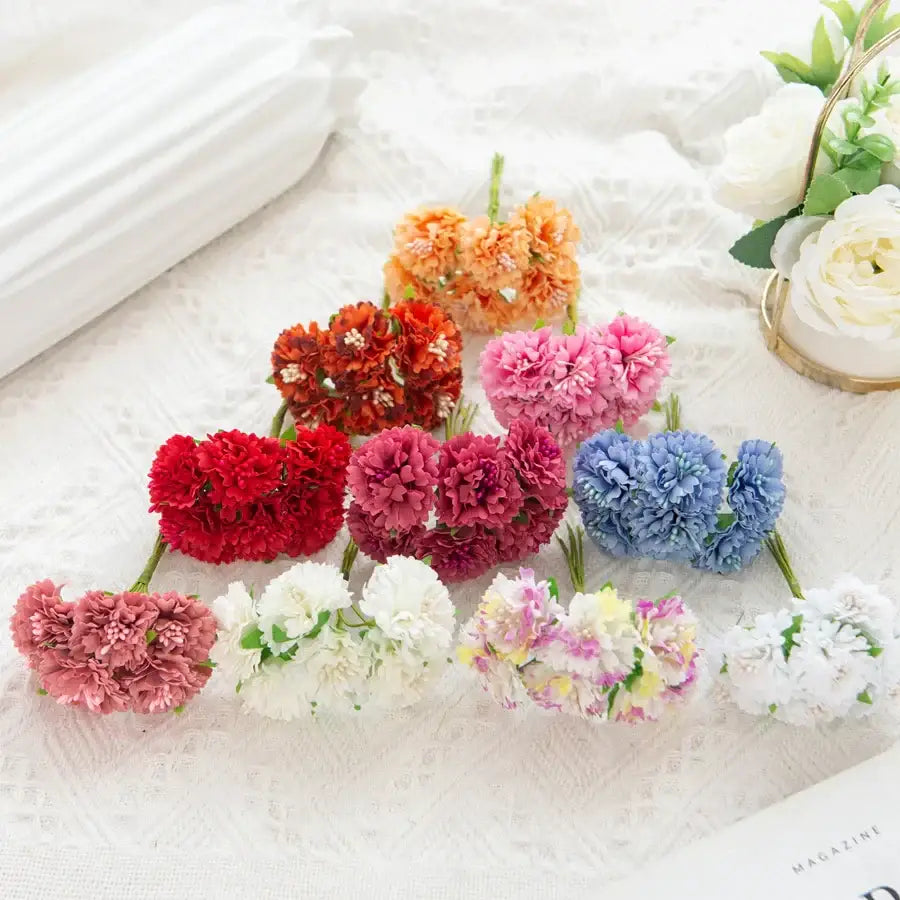 A collection of vibrant red pink orange blue and white decorbites carnation stamen silk flowers on lace surface