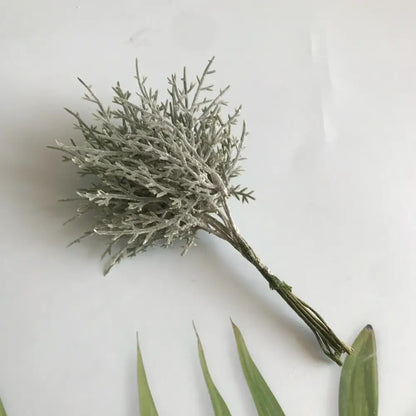 A delicate silvery-gray artificial plant with feathery branches in a vibrant multicolored dried flower bouquet in white vase