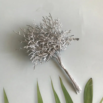 Silver metallic branch brooch with intricate twig detailing displayed alongside vibrant dried flower bouquets in white vase