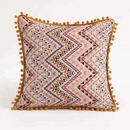 A square pillow cover with beige base and geometric rust black patterns accented by mustard pom poms for ethnic boho decorbites throw decor