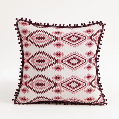 A vibrant ethnic boho throw pillow cover with white base pink maroon geometric patterns and dark red pom-pom trim decorbites