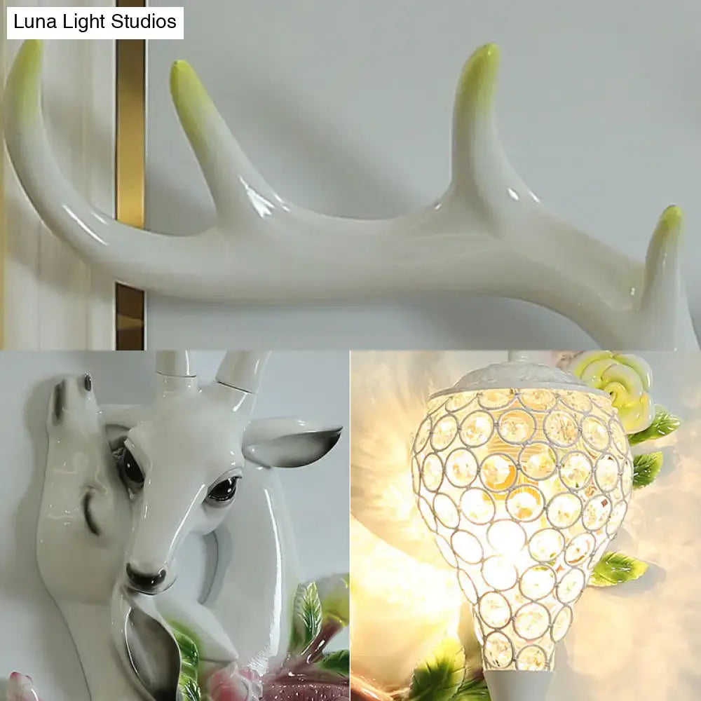 White ceramic deer head accent wall sconce with glossy finish and crystal lampshade emitting warm bedroom light