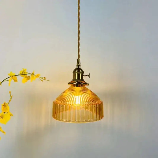 A warm amber colored glass pendant light with vertical ridges and brass-finished metal fixture for dining room