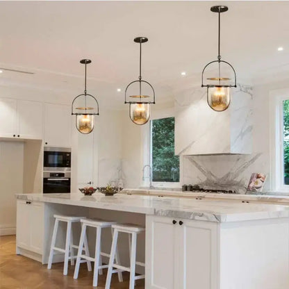 Three vintage amber glass pendant lights with brass accents illuminate a modern kitchen island as glass pendant lights
