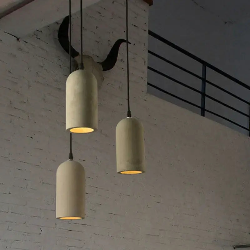 Three vintage beige decorbites cement pendant lamps hang with warm glowing interiors against white brick wall