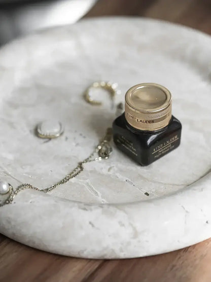 A sleek black estée lauder serum bottle with gold cap on a vintage beige travertine serving tray decorbites beige travertine