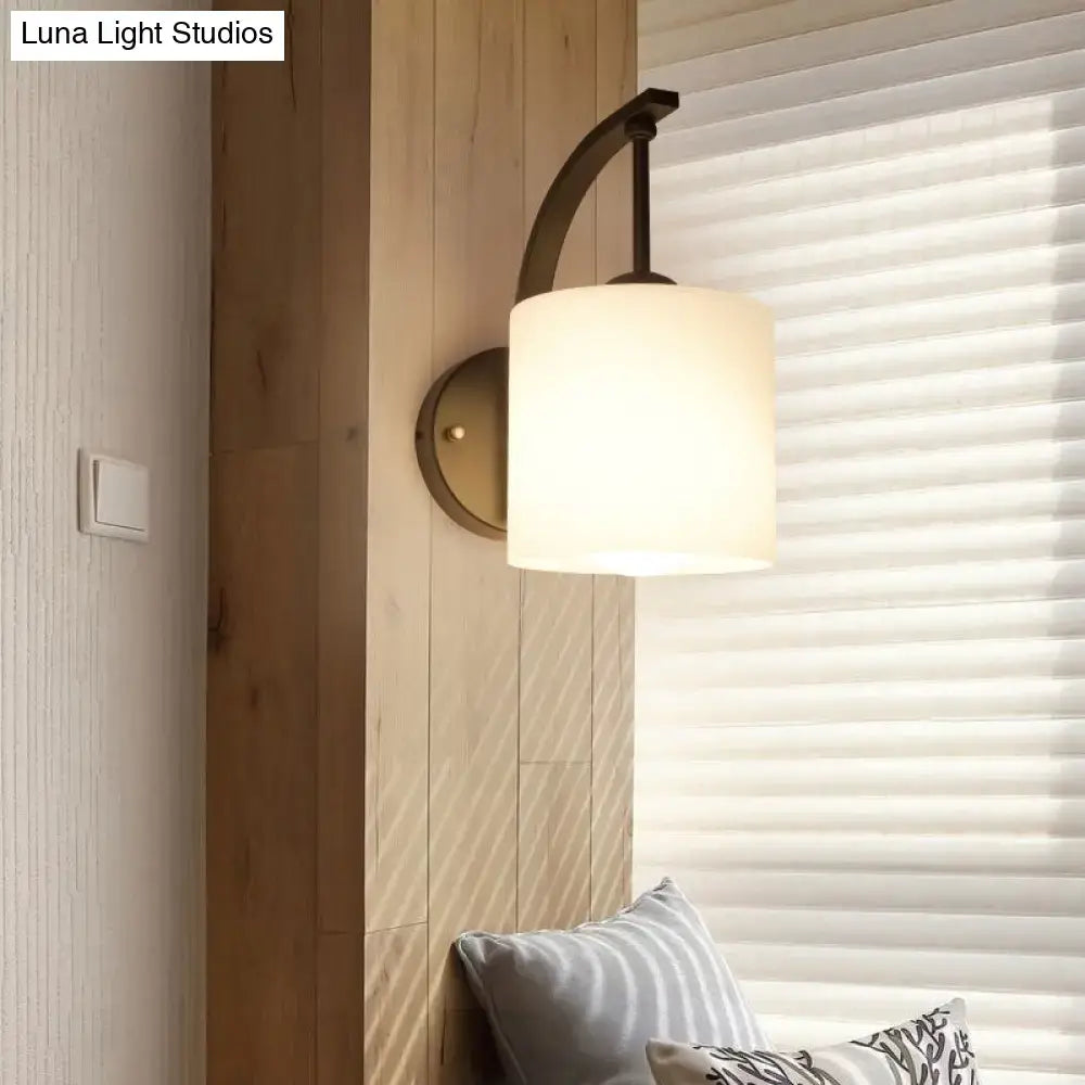A vintage black glass wall lamp fixture type with a curved dark metal arm and cylindrical frosted glass shade bulb base