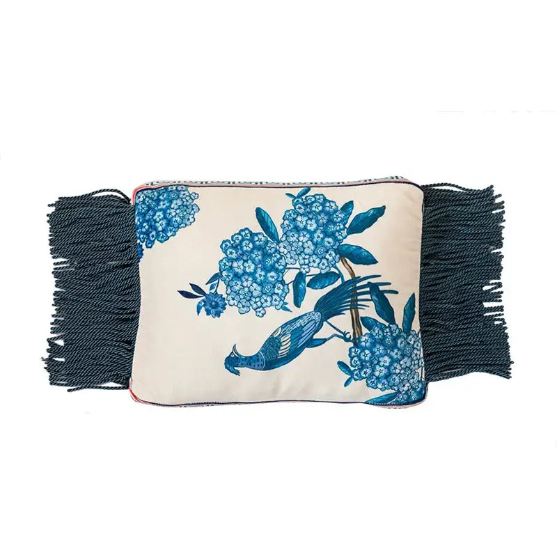 Cream-colored cushion case with blue peacock toile floral and bird design and dark navy fringe for living room use