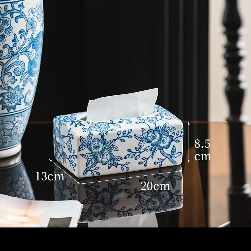 A rectangular white porcelain tissue box with intricate blue floral patterns and a tissue partially pulled out for living room decor