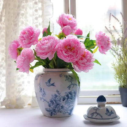 A vintage blue white porcelain vase with blue floral and bird motifs holds vibrant pink peonies for living room decor