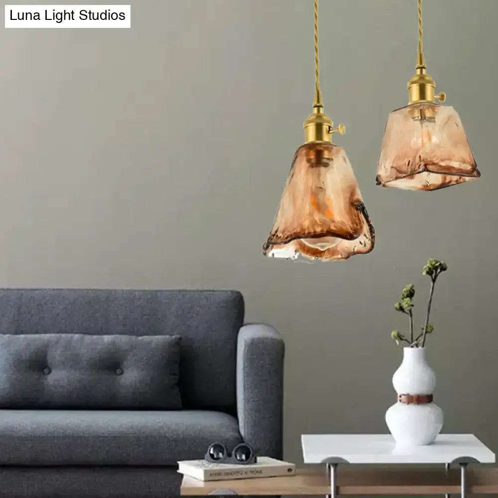 Two amber-tinted handmade glass pendant lights with brass shaded drop fixtures hang from twisted gold cords