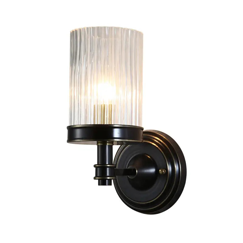Vintage brass and black wall lamp with clear ribbed glass cylinder shade providing warm bedroom lighting