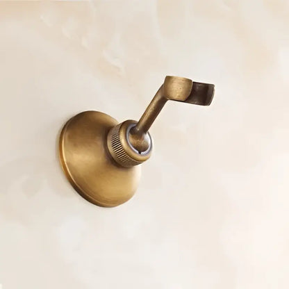 Antique brass wall-mounted towel rack with curved hook and circular base complementing handheld shower head fixture