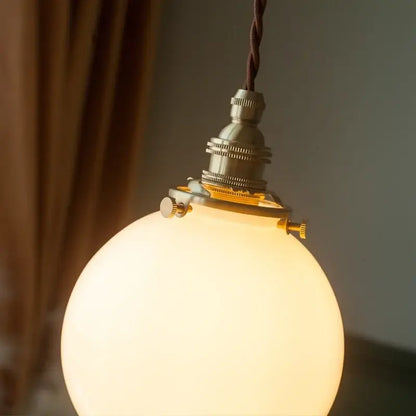 Vintage brass and cream glass ball pendant light with warm-toned decorbites cream glass and twisted brown cord