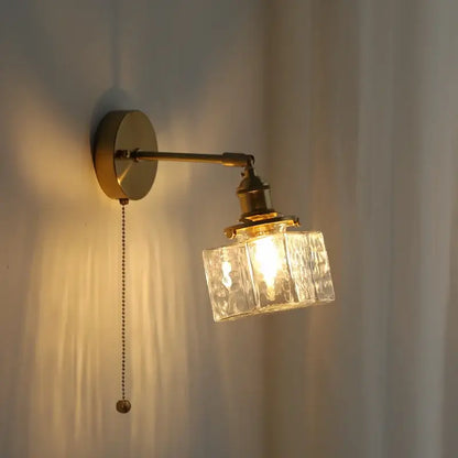 Vintage brass and glass led wall lamp with a textured clear glass cube shade and pull chain for bedroom use