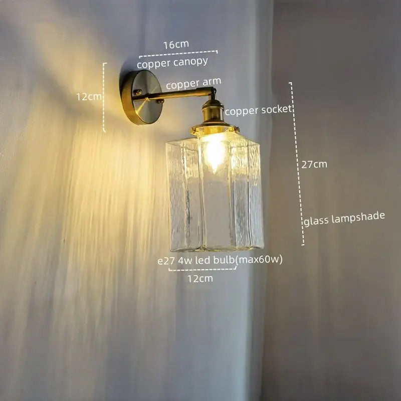 A vintage brass and glass led wall lamp with a warm-toned copper arm and textured clear glass shade for bedroom use